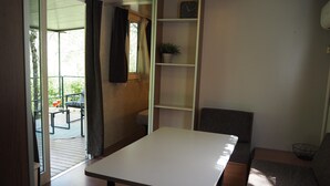 A room with a white table, a grey sofa, a bookshelf, and a window with curtains. - Tuscan Mobile Home With Covered Porch (Bucine)
