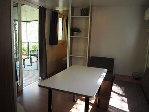 Ein Zimmer mit einem weißen Tisch, einem grauen Sofa, einem Bücherregal und einem Fenster mit Vorhängen.