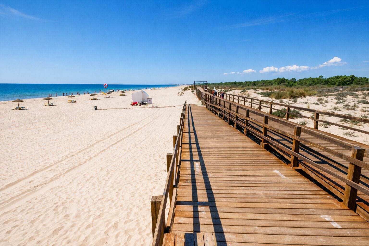 Een houten looppad dat naar een zandstrand leidt, met parasols en strandstoelen.