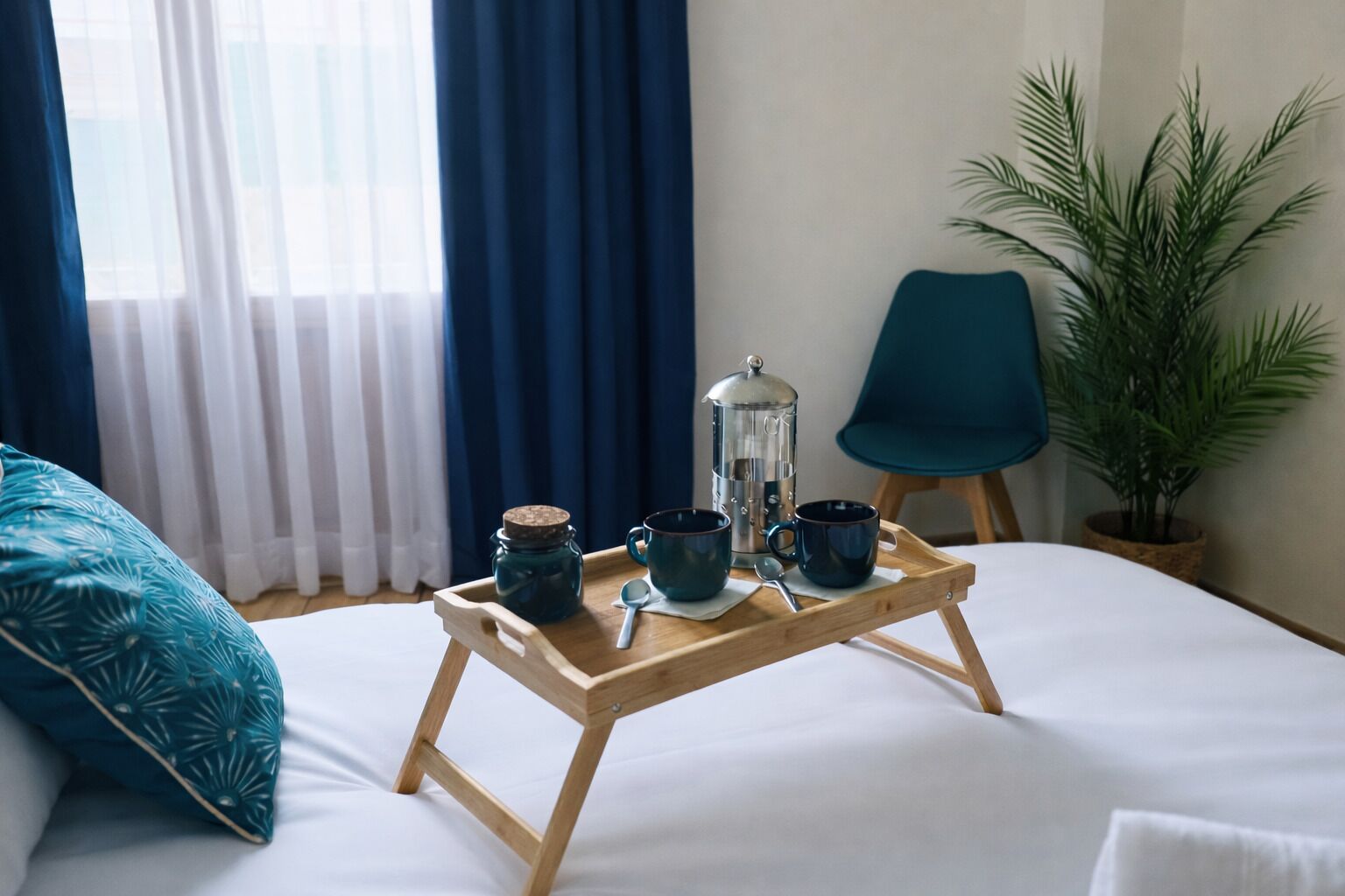 A bed with a wooden tray holding a coffee pot, two mugs, and a jar.