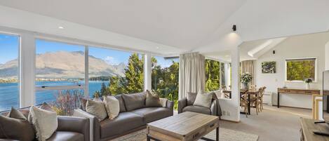 A modern living room with a large window, a sofa set, a coffee table, and a dining area.