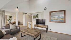 Una sala de estar moderna con un sofá, una mesa de centro, un televisor y vistas a montañas a través de una ventana.