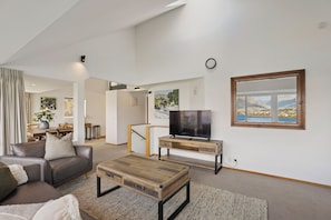 Ein modernes Wohnzimmer mit einer Couch, einem Couchtisch, einem Fernseher und Blick auf Berge durch ein Fenster.