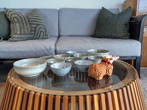 Ein modernes Wohnzimmer mit einem runden Glastisch, einer grauen Couch und dekorativen Kissen.