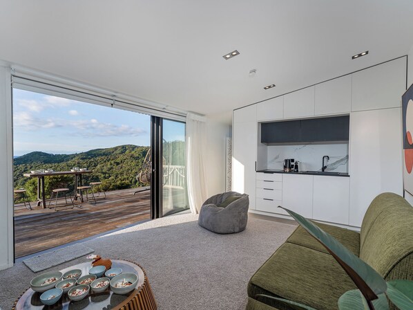 Eine moderne Küche mit Blick auf eine bewaldete Landschaft, ein Essbereich mit Tisch und Stühlen sowie eine gemütliche Sitzecke mit Sitzsack.