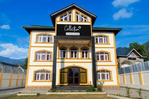 A multi-story building with a prominent entrance and a sign indicating it is company-serviced. - Deluxe Pine Hills (Srinagar)