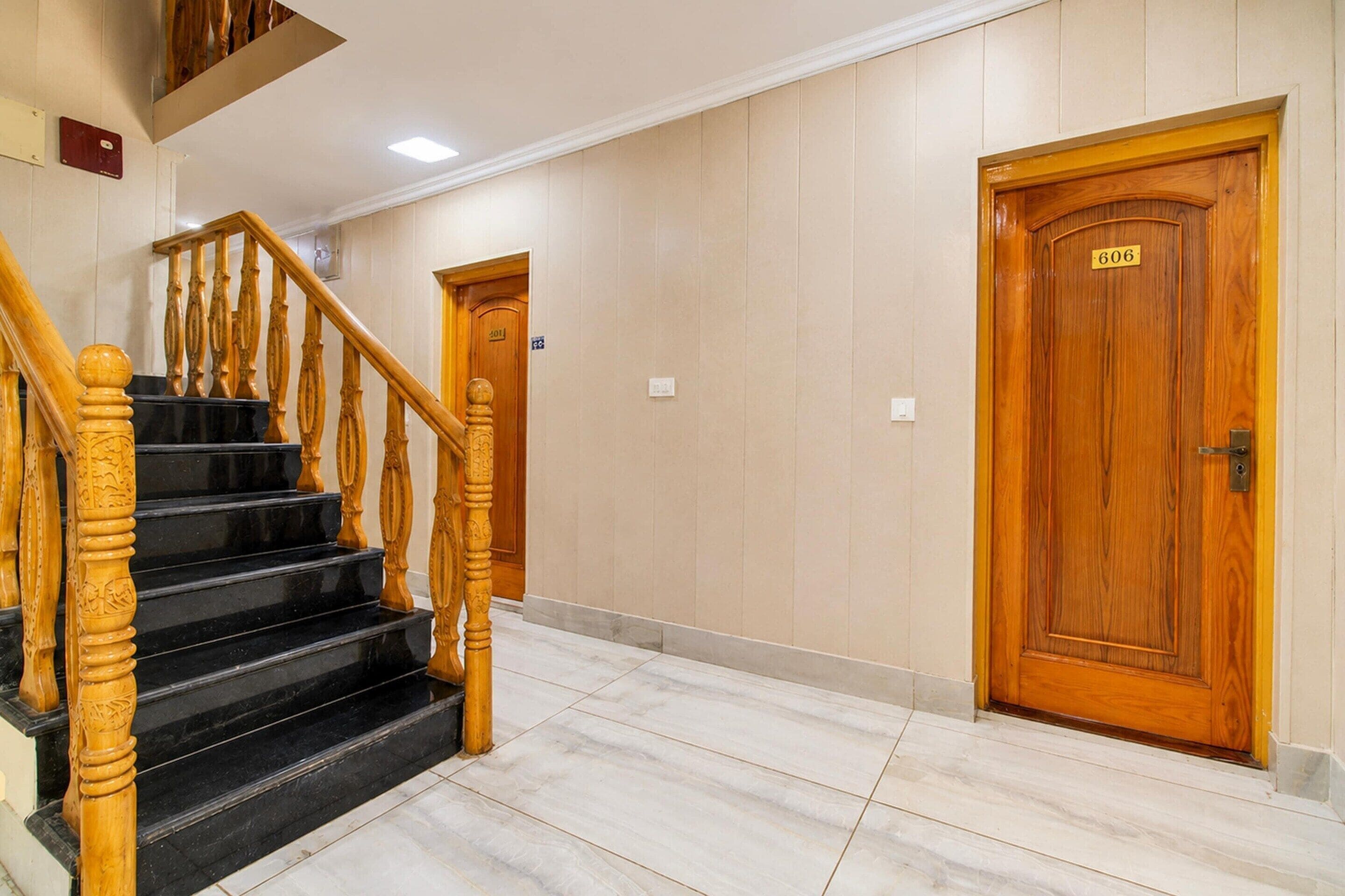 A staircase with wooden balusters leading to a landing, a wooden door with a number plate, and a wall with a light switch.