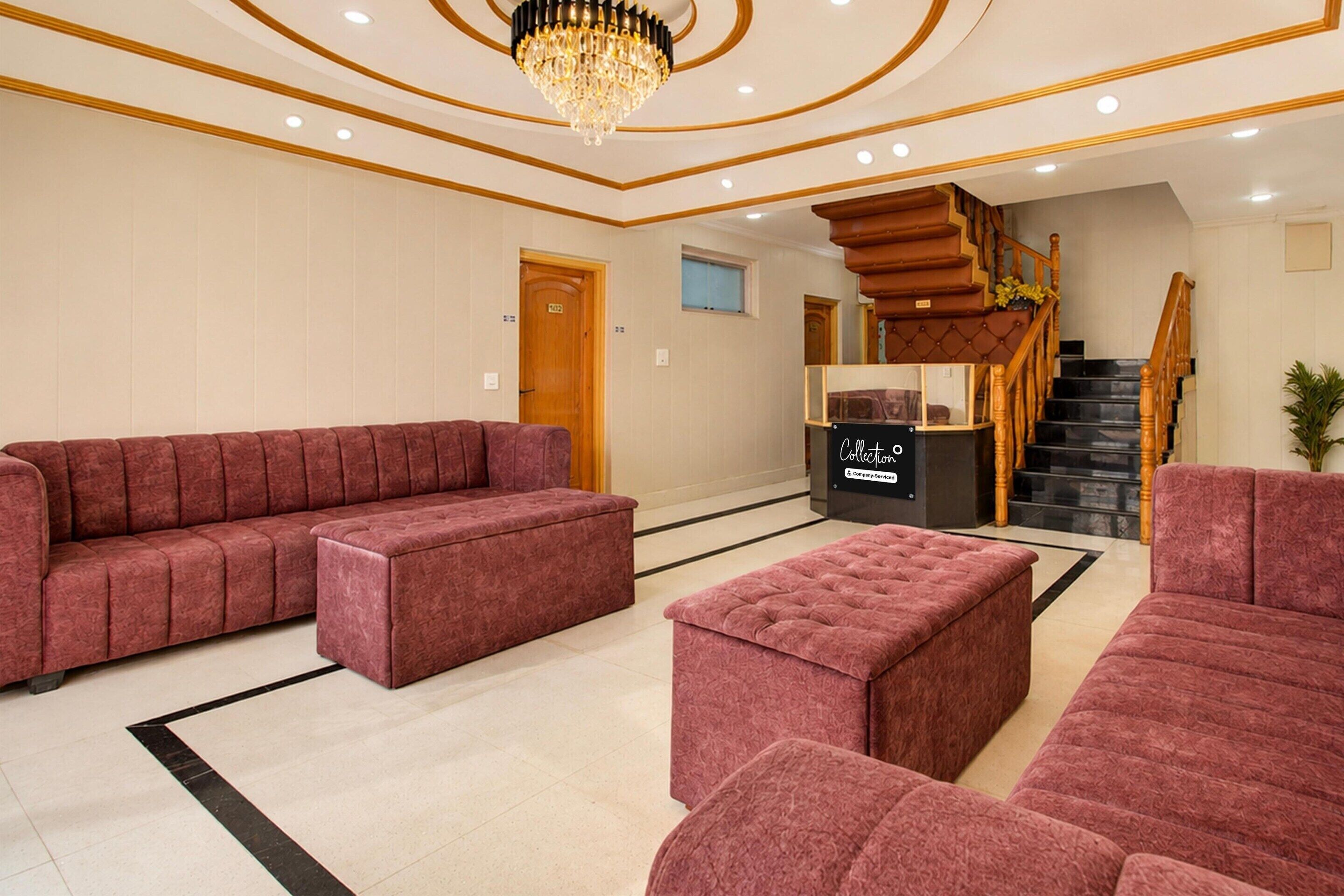 A spacious lobby with a large red sofa, a smaller red ottoman, and a black and gold chandelier.