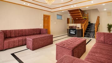 A spacious lobby with a large red sofa, a smaller red ottoman, and a black and gold chandelier.