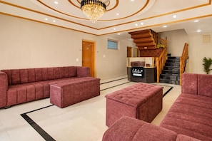 A spacious lobby with a large red sofa, a smaller red ottoman, and a black and gold chandelier. - Deluxe Pine Hills (Srinagar)