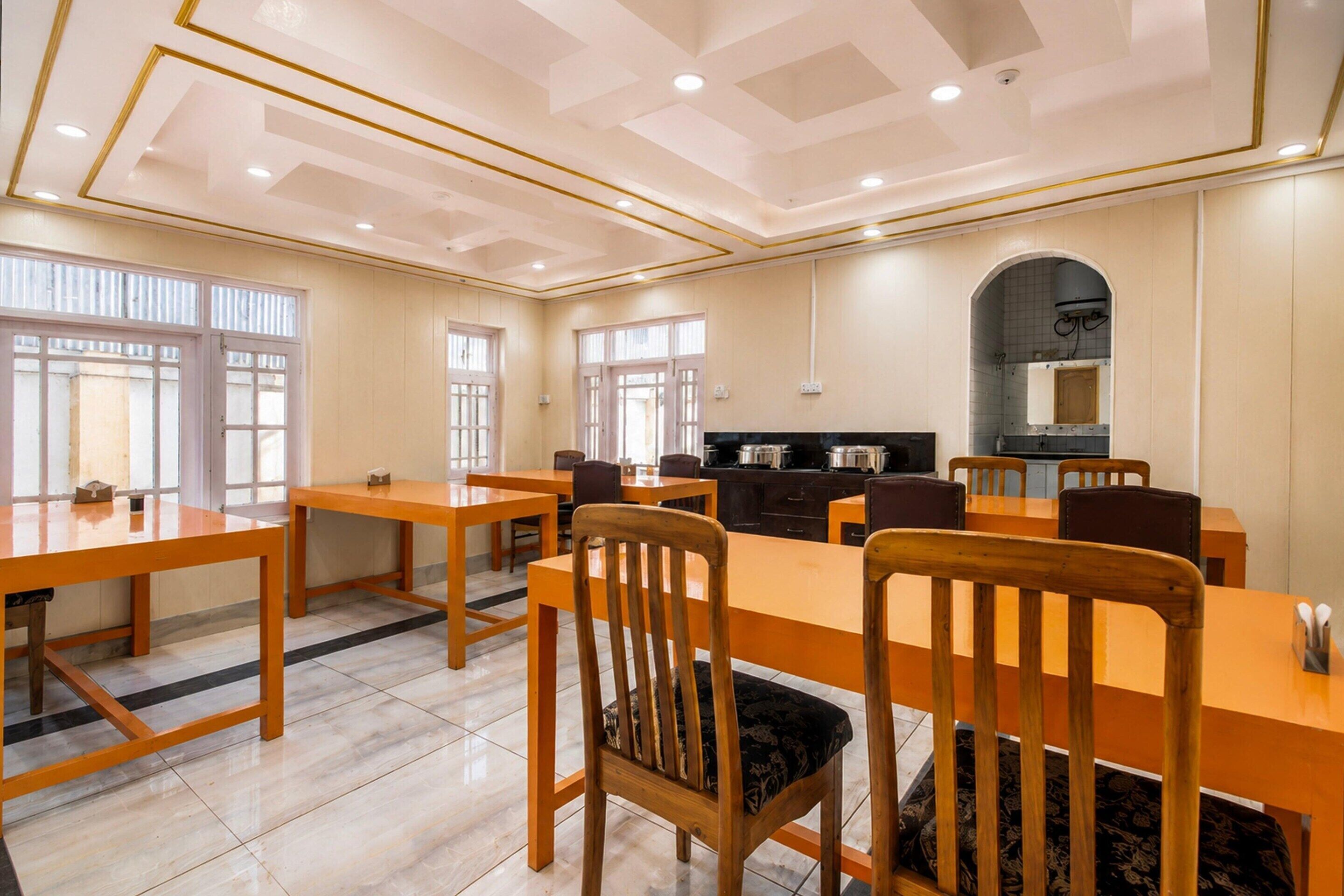 A spacious dining area with multiple tables and chairs, a kitchen area with appliances, and large windows allowing natural light.