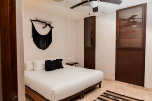 A bedroom with a bed, a ceiling fan, a wooden door, and a wall-mounted decoration. - Bajo Cielo: Jungle-View Terrace with Private Pool (Tulum)