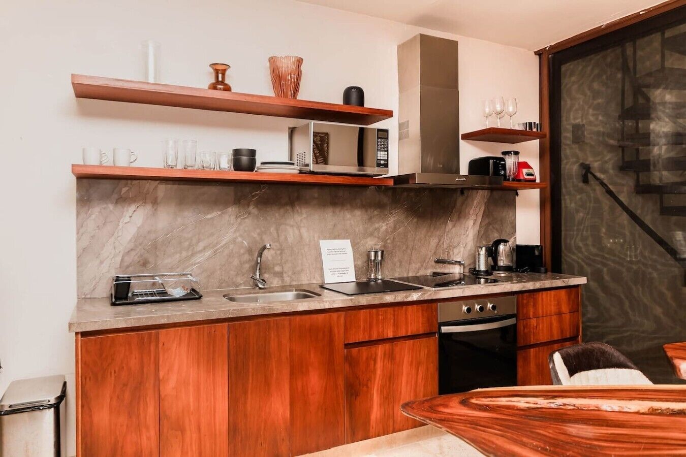 A modern kitchen with wooden cabinets, a marble countertop, a built-in oven, and a coffee machine.