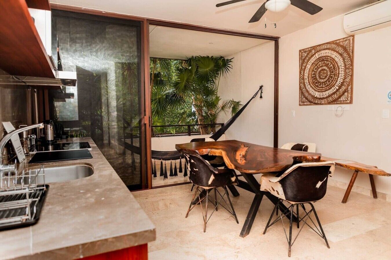 A kitchen with a dining area, a sliding glass door leading to a balcony with plants, and a ceiling fan.