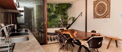 A kitchen with a dining area, a sliding glass door leading to a balcony with plants, and a ceiling fan.