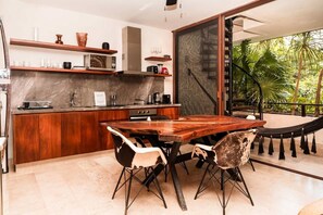 A modern kitchen with a wooden table and chairs, a built-in oven, and a view of a lush garden through a glass door. - Bajo Cielo: Jungle-View Terrace with Private Pool (Tulum)