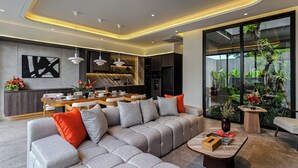Ein modernes Wohnzimmer mit Ecksofa, Esstisch und Blick auf einen Garten durch große Fenster.