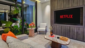 Ein modernes Wohnzimmer mit einem großen Flachbildfernseher, einem bequemen Sofa, einem kleinen Tisch und einer Zimmerpflanze.