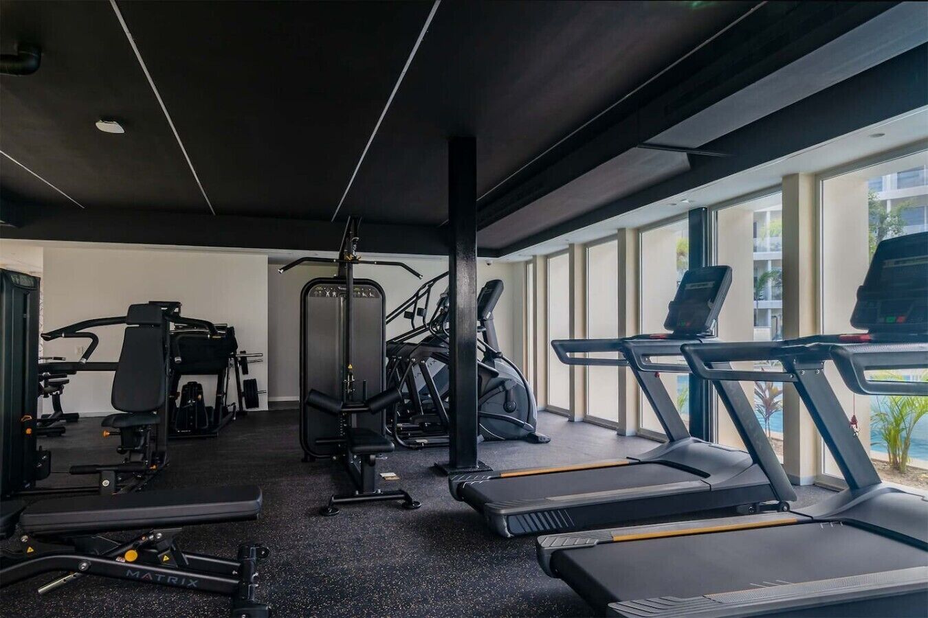 Ein Fitnessstudio mit Laufbändern, Kraftgeräten und einem an der Wand befestigten Crosstrainer.