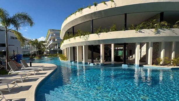 A modern hotel with a curved pool, lounge chairs, and a clear blue sky. - Stylish Apt with Private Balcony, Pool and Gym (Playa del Carmen)