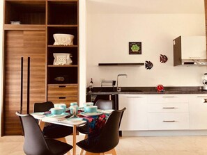 Une cuisine moderne avec des meubles blancs, un plan de travail noir et un coin repas avec une table dressée pour quatre personnes.