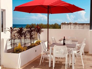 Eine Terrasse mit Tisch, Stühlen und einem roten Sonnenschirm.