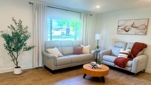 Ein geräumiges Wohnzimmer mit zwei Sofas, einem Couchtisch, einer Topfpflanze und einem Fenster mit Vorhängen.