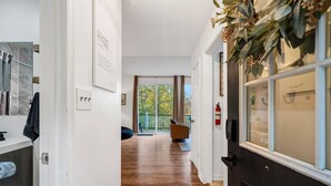 Un pasillo con suelo de madera, una puerta con ventanal y vistas a un balcón con una silla.