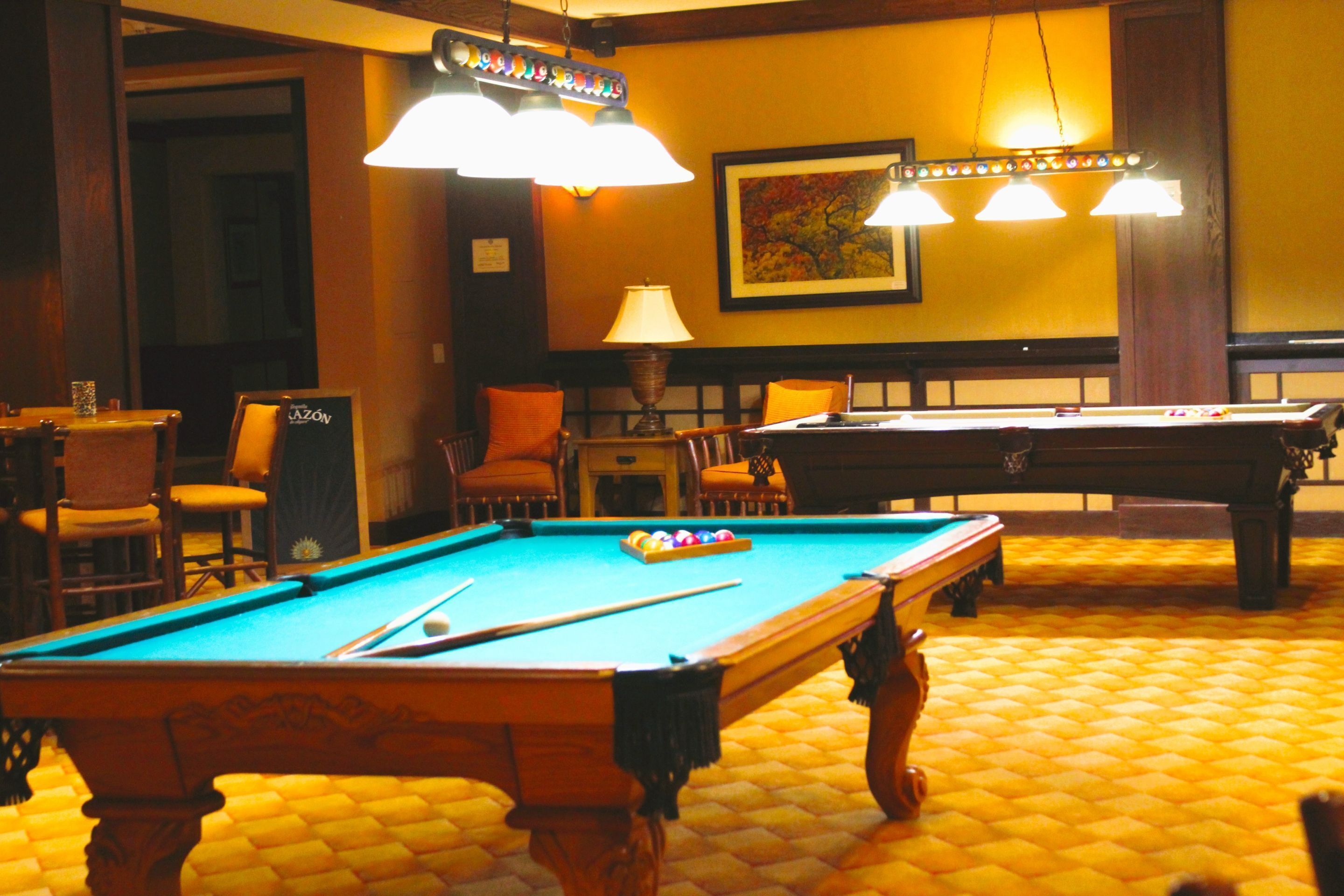 A billiards room with a pool table, chairs, and a lamp.