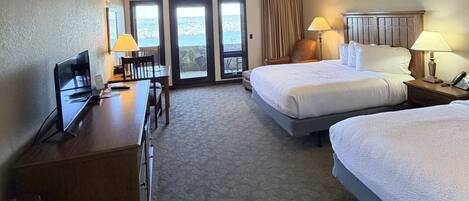 Quarto de hotel com duas camas, uma mesa com computador, uma cadeira e uma luminária.