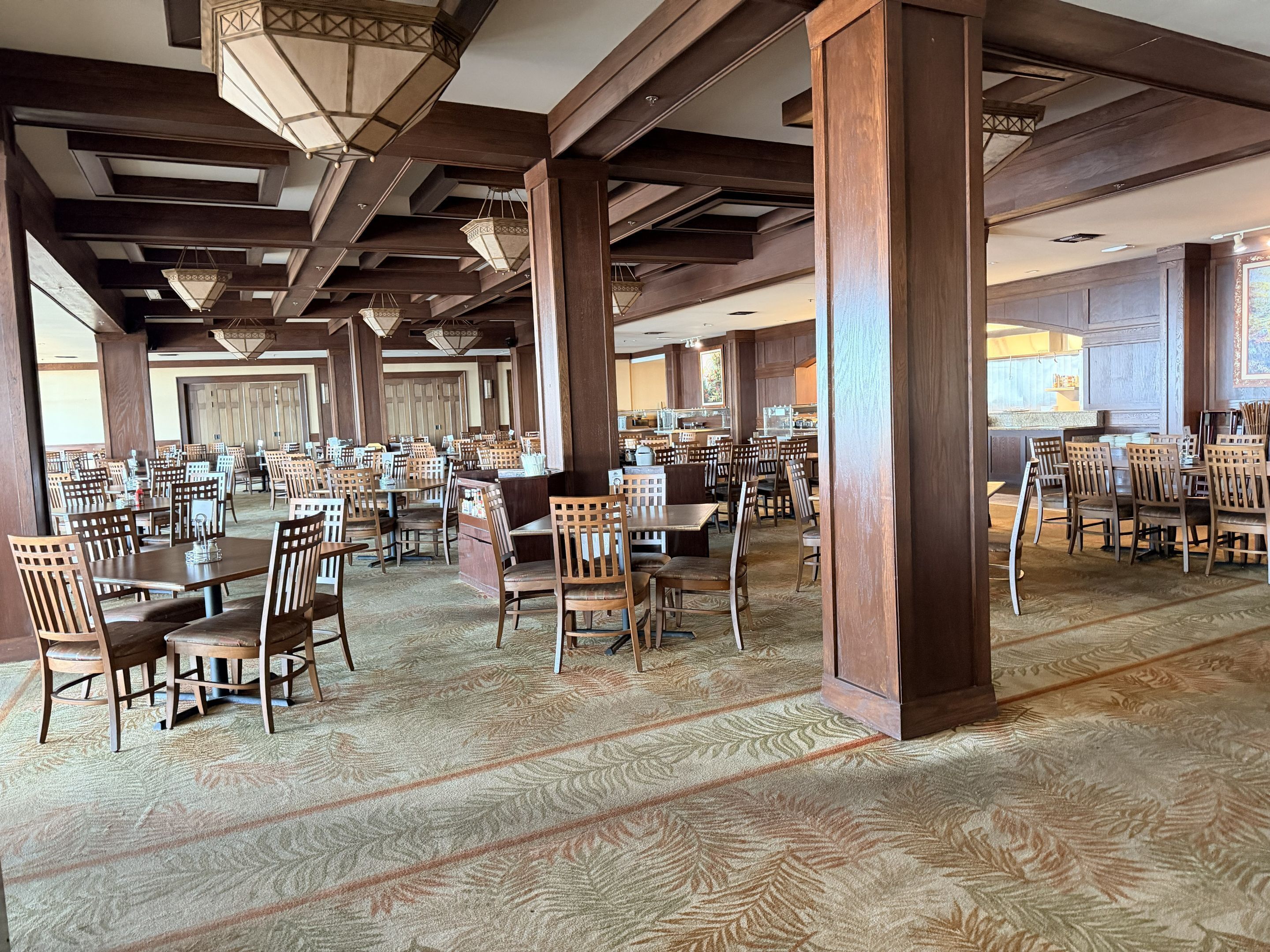 A spacious dining area with high wooden beams, multiple tables, and chairs.