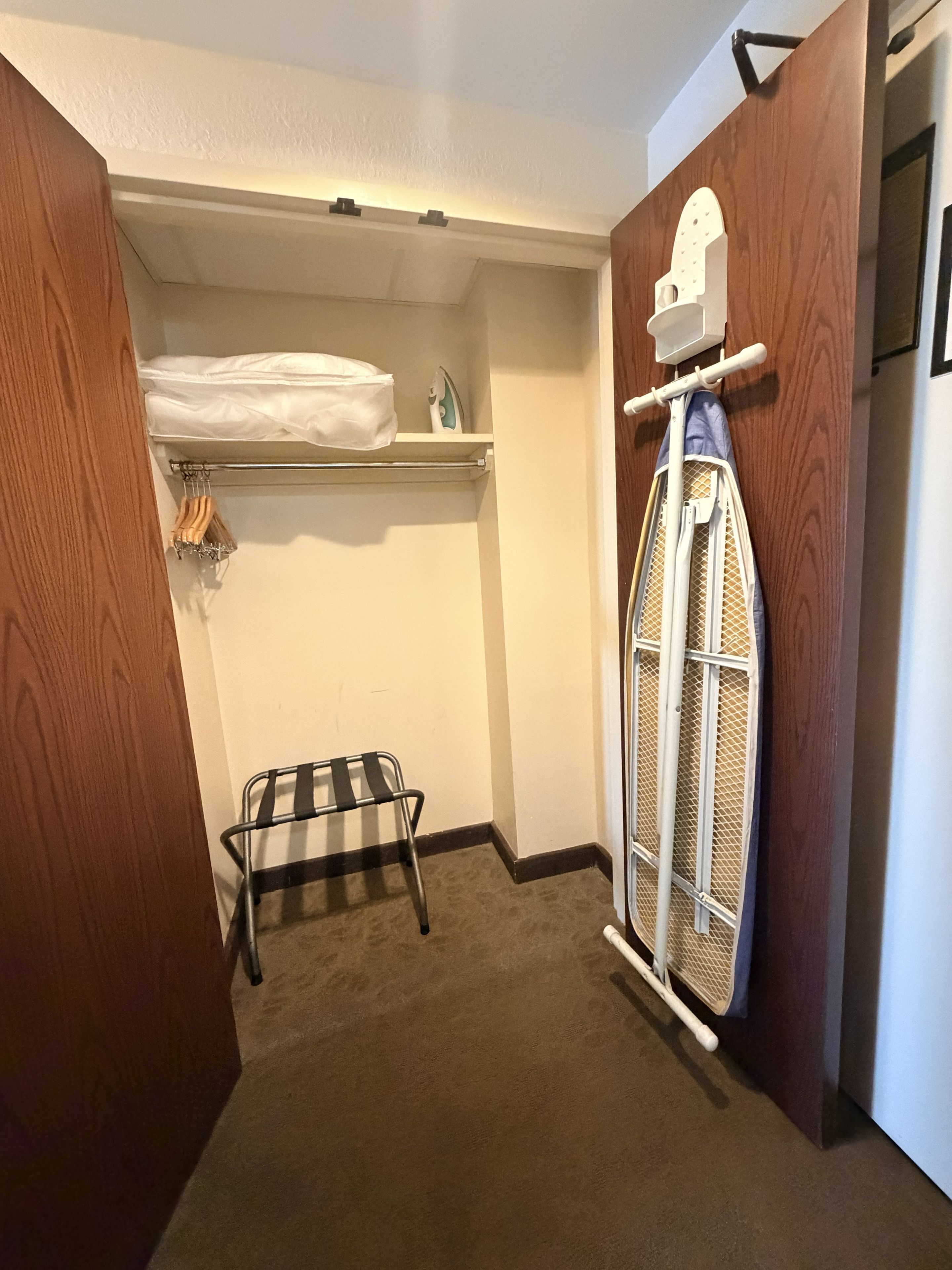 A small laundry room with a drying rack, ironing board, and a shelf with folded clothes.