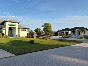 A residential area with two houses, a well-maintained lawn, and a clear sky. - Gorgeous 3-bedroom house with Heated Pool and Spa (Cape Coral)