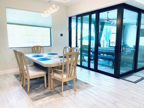 A dining area with a table set for six, wooden chairs, a rug, and a view through a glass door to an outdoor patio. - Gorgeous 3-bedroom house with Heated Pool and Spa (Cape Coral)