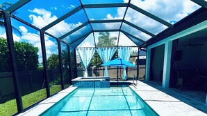 A covered outdoor swimming pool with a clear view of the sky and a fenced backyard. - Gorgeous 3-bedroom house with Heated Pool and Spa (Cape Coral)