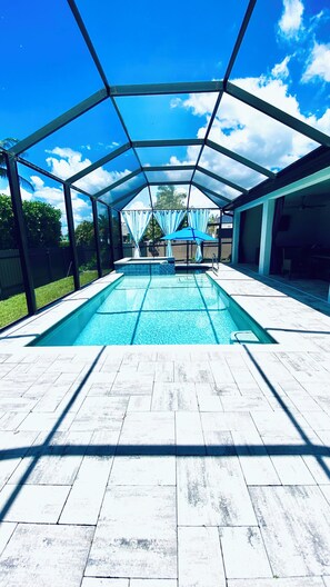 A covered outdoor swimming pool with a clear view of the sky and a fenced backyard. - Gorgeous 3-bedroom house with Heated Pool and Spa (Cape Coral)