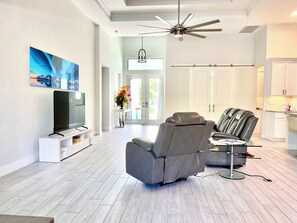 A modern living room with a flat-screen TV, a reclining chair, and a ceiling fan. - Gorgeous 3-bedroom house with Heated Pool and Spa (Cape Coral)
