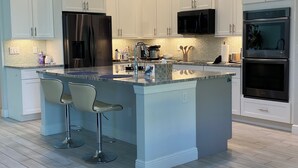 A modern kitchen with white cabinets, stainless steel appliances, and a central island with bar stools. - Gorgeous 3-bedroom house with Heated Pool and Spa (Cape Coral)