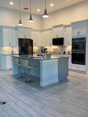 A modern kitchen with white cabinets, stainless steel appliances, and a central island with bar stools. - Gorgeous 3-bedroom house with Heated Pool and Spa (Cape Coral)