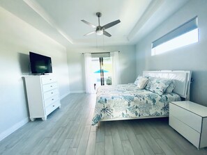 A bedroom with a bed, a TV, a ceiling fan, a dresser, and a window. - Gorgeous 3-bedroom house with Heated Pool and Spa (Cape Coral)