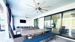 A sunlit patio with a wooden table, blue cushioned seating, and a ceiling fan. - Gorgeous 3-bedroom house with Heated Pool and Spa (Cape Coral)