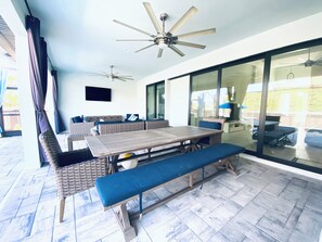A sunlit patio with a wooden table, blue cushioned seating, and a ceiling fan. - Gorgeous 3-bedroom house with Heated Pool and Spa (Cape Coral)