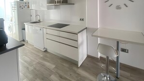 A modern kitchen with white cabinetry, a stainless steel sink, a built-in oven, and a wall clock.