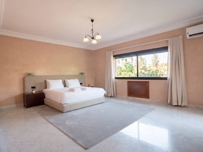 A hotel room with a large bed, a nightstand, a bedside table, a window with curtains, and a ceiling light fixture. - Villa Zitouna: Luxury Golf, Pool, and Garden in Amelkis + Free Airport Transfer  (Marrakech)