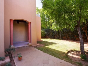 A building entrance with a covered porch, a small garden area with grass and a tree, and a potted plant. - Villa Zitouna: Luxury Golf, Pool, and Garden in Amelkis + Free Airport Transfer  (Marrakech)