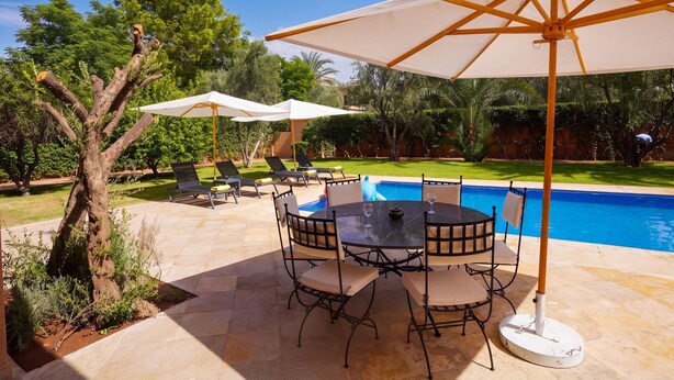 Een terras buiten met een zwembad, lounge stoelen en parasols.