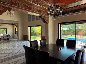 A spacious room with a large dining table, leather chairs, a chandelier, and a view of a swimming pool. - Villa Zitouna Luxury Golf & Pool & Garden Amelkis (Marrakech)