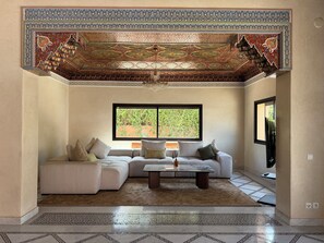 A living room with a sectional sofa, a coffee table, patterned rugs, and a decorative ceiling. - Villa Zitouna Luxury Golf & Pool & Garden Amelkis (Marrakech)