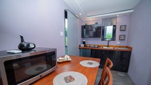 Ett kompakt kök med en mikrovågsugn, ett träbord med underlägg, en stol och en tv som är monterad ovanför bänkskivan.