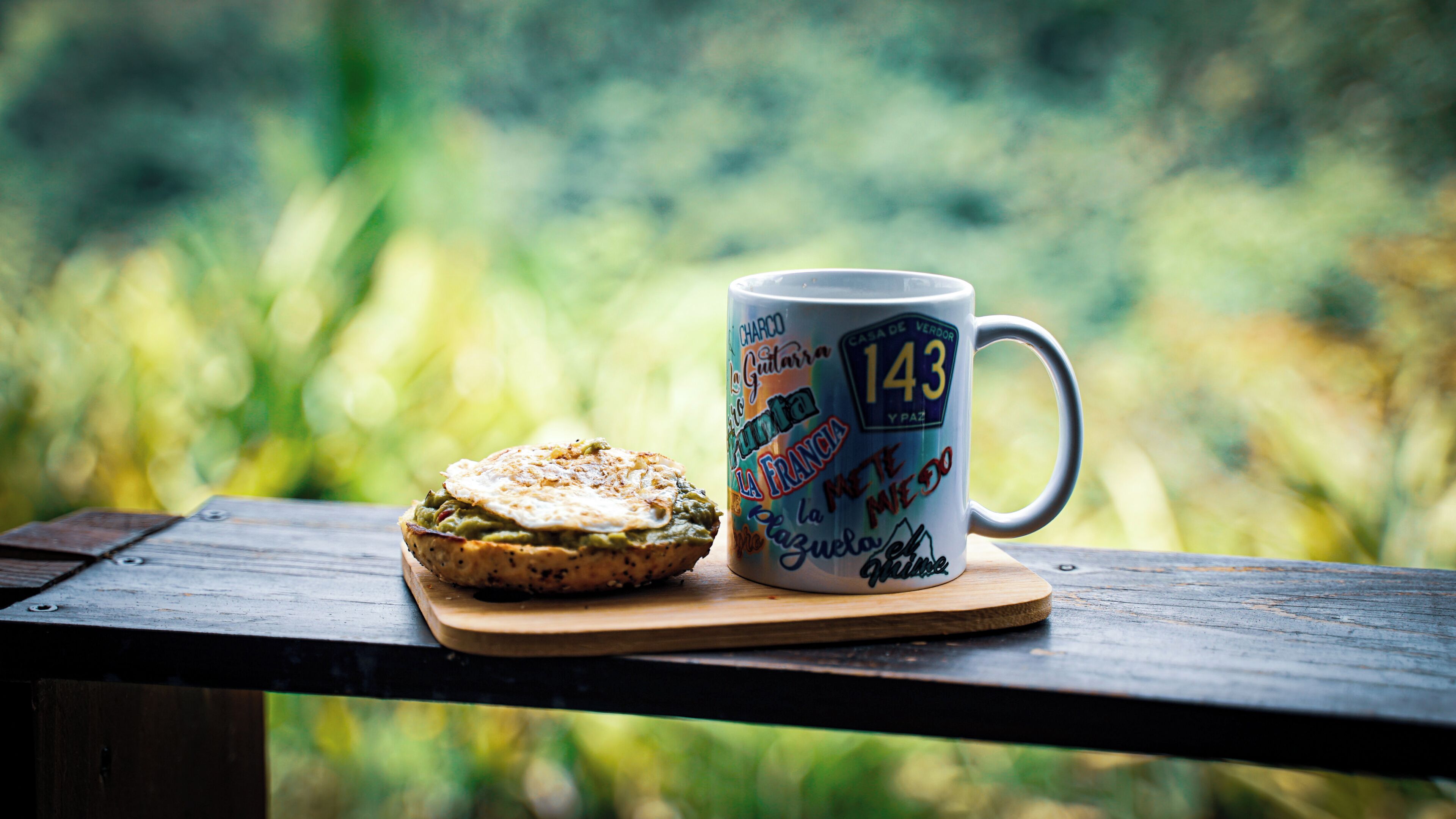 A mug with a number and text, a sandwich, and a blurred green background.